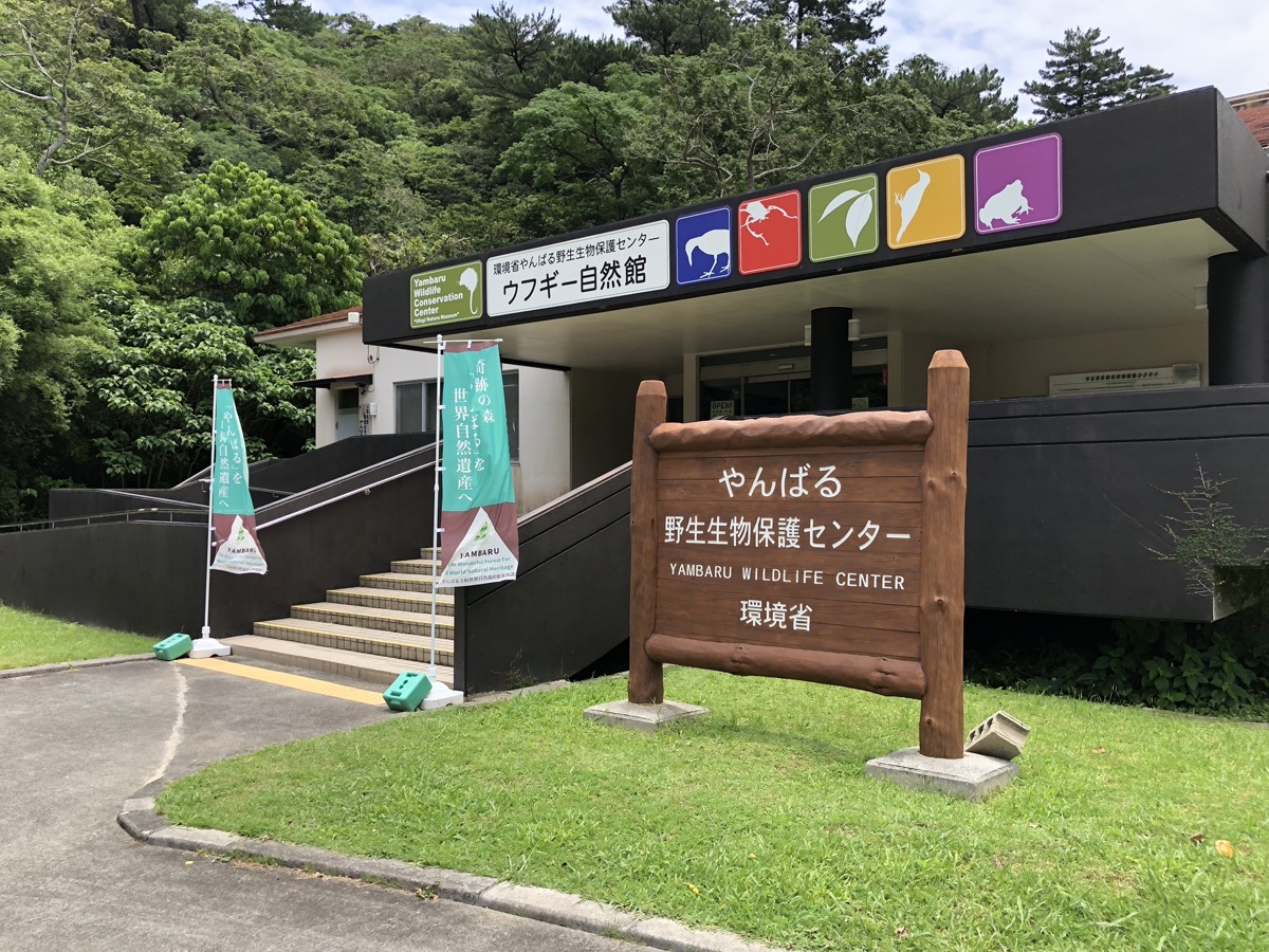 Entrance to the Yambaru Wildlife Conservation Center in northern Okinawa, with bilingual Japanese and English signage and a stone walkway leading toward the building.